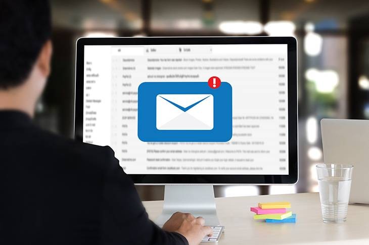 Hombre de espaldas con bandeja de correo abierta en su monitor y alerta de mensaje de entrada