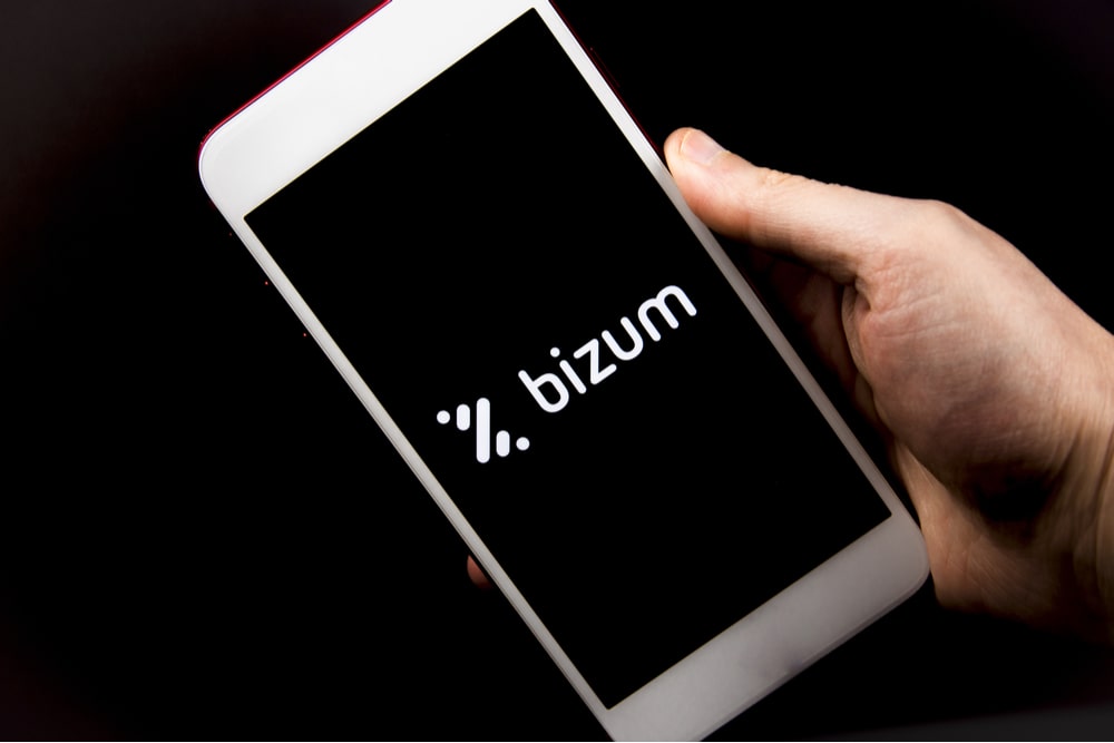 Mano de hombre sujetando un teléfono con logo de Bizum sobre fondo negro