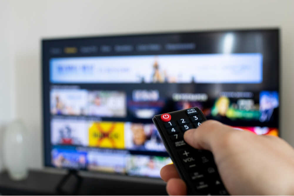 Mano derecha masculina seleccionando contenido en streaming en televisor