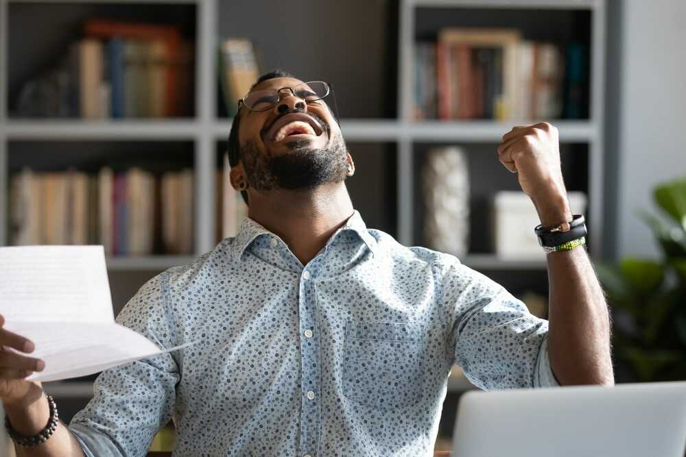 Hombre joven celebrando una noticia en su despacho ante el ordenador
