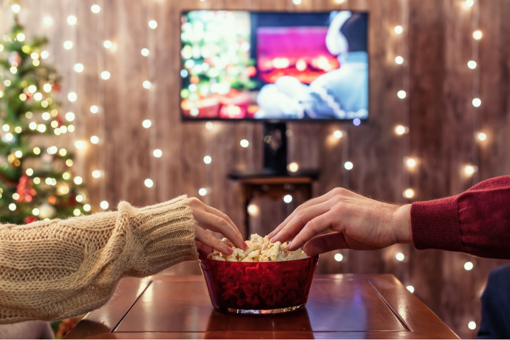 Dos brazos cogiendo palomitas de un bol mientras ven televisión en un salón con decoración navideña