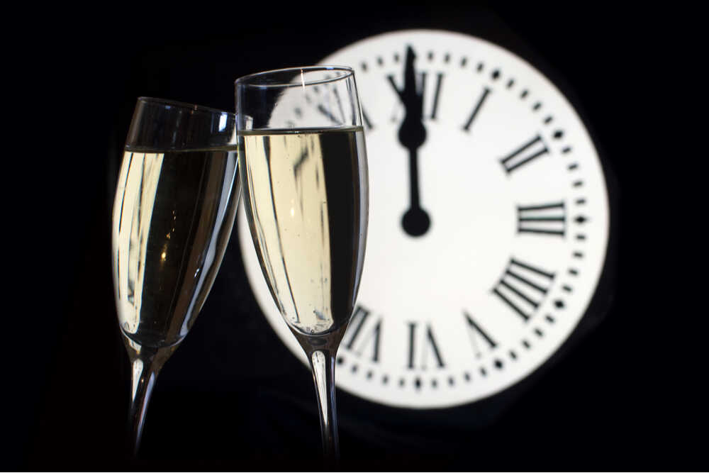 Reloj de números romanos marcando las 12:00 h con copas de champán en primer plano
