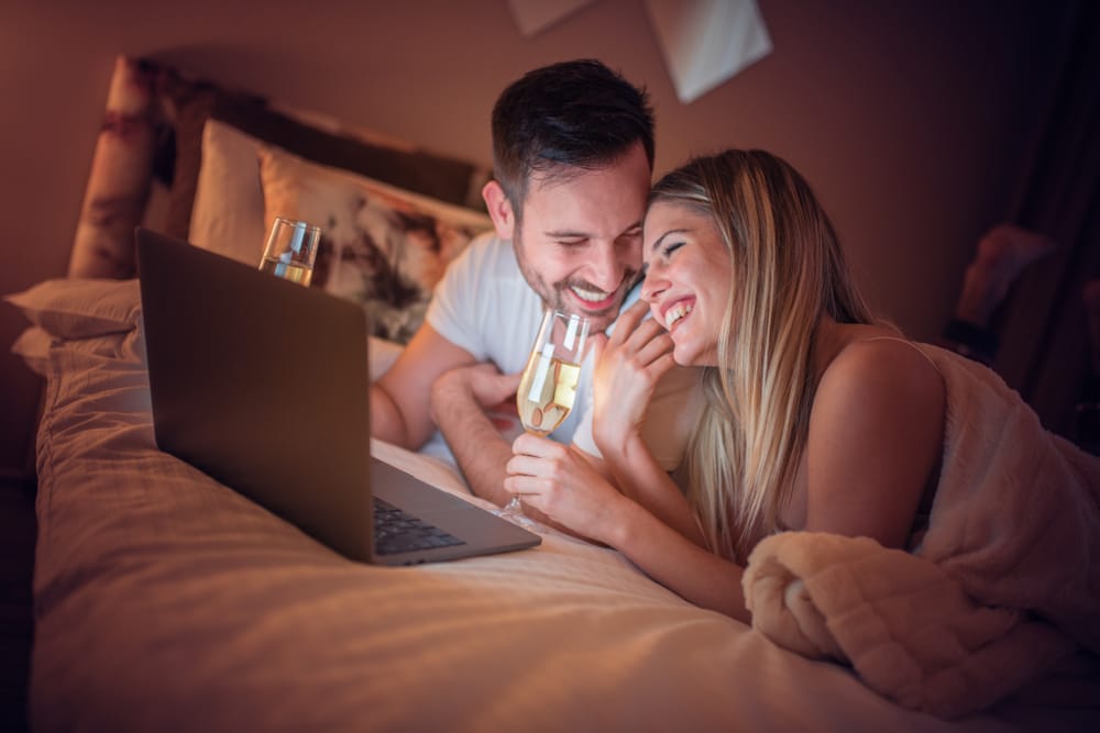 pareja-viendo-ordenador-cama-champan