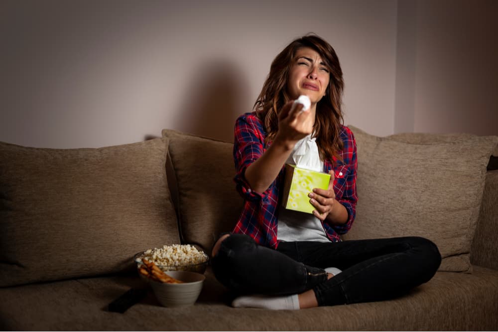 Mujer joven emocionada en el sofá mientras ve la televisión y come snacks