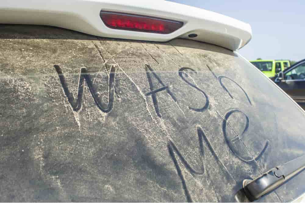 Luna trasera de coche sucio con una nota en inglés: "wash me" o "lávame"