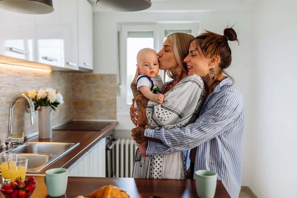 Pareja de madres tatuadas con un bebé en brazos en la cocina