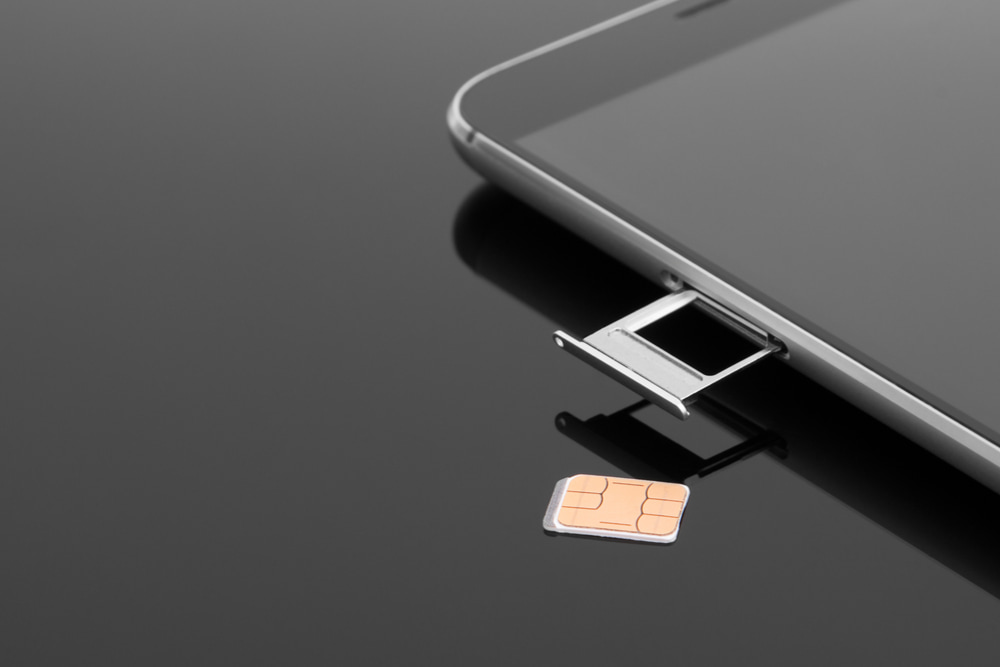 Smartphone negro sobre fondo negro con tarjeta SIM al lado y bandeja SIM abierta